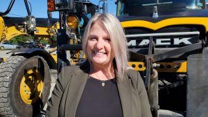 A woman stands in front of a parked dump truck